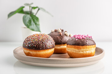 assorted chocolate glazed donuts on ceramic plate and home plant on white glass surface close up