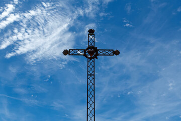 Iron cross depicting the sacred heart of Jesus on a sunny blue sky background. Croix de fer repr&eacute;sentant le c&oelig;ur sacr&eacute; de J&eacute;sus sur fond de ciel bleu ensoleill&eacute;.