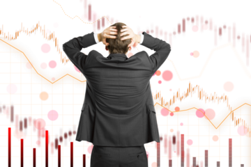 A person in a suit clutching their head with financial graphs in the background, representing stress or loss