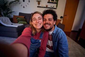 Happy selfie of a caucasian young couple at home using smartphone to take a cheerful photography...