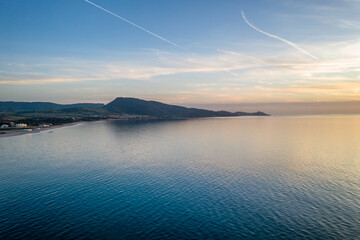 Drone aerial view of San Pietro a Mare wild beach coast with Castelsardo on the background at sunset in Sardinia, Italy