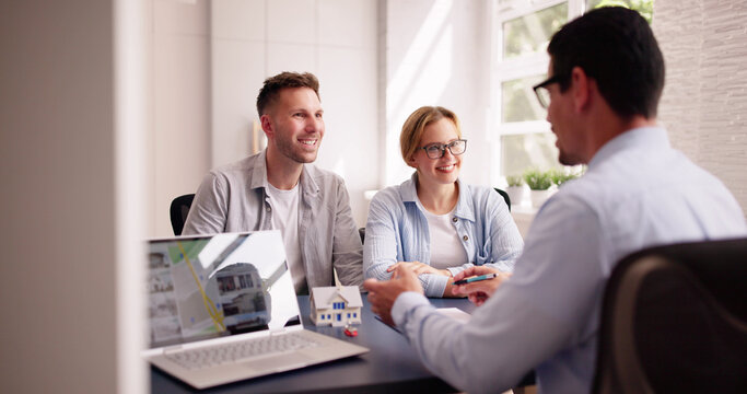 Young Hispanic businessman showing house picture on laptop to happy couple