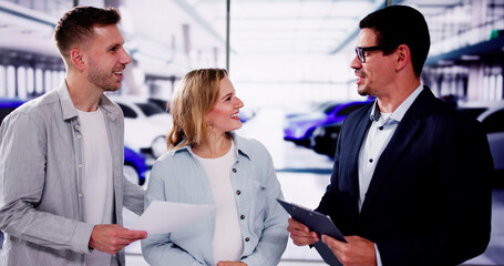 Young couple smiling and talking to salesman at dealership, interested