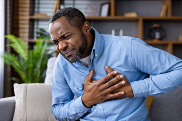 Man in blue shirt clutching his chest in pain, possibly experiencing a heart attack or cardiac arrest. The image shows clear signs of distress and urgent need for medical assistance.