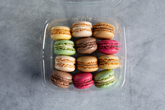A top down view of a box of assorted macaron cookies in a plastic clamshell container.