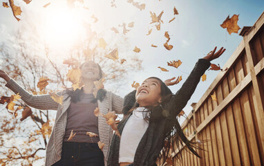 Autumn, mother and daughter throwing leaves in garden of home together for bonding or love. Asian family, fall or season with single parent woman and girl child having fun in backyard for wellness