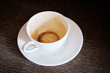 An empty cup after drinking coffee on the table. A white cup on a dark table. Selective focus