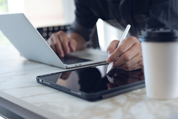 Close up of man using stylus pen on diigtal tablet pc and working on laptop computer on table. man...