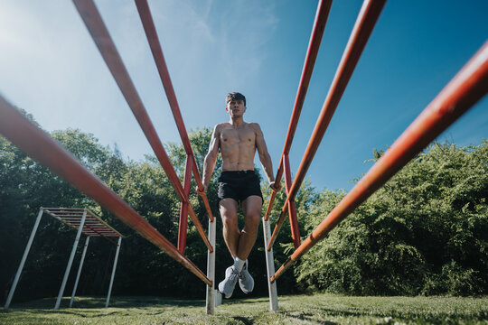 Athletic young man performing exercises on parallel bars in an urban park, showcasing strength and fitness on a sunny day.