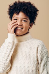 A young african american boy in a white sweater covering his face with his hand, expressing shyness...