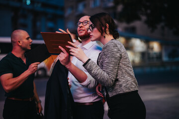 Three entrepreneurs using digital tablets, engaged in a serious discussion and strategizing together outdoors in an urban environment.