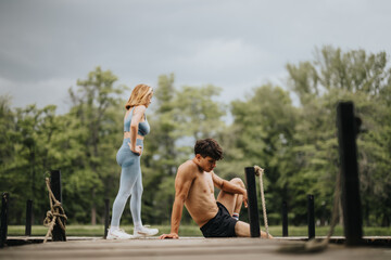 Obraz premium Man and woman performing outdoor exercise on a wooden pier surrounded by greenery, focusing on fitness and wellness in a natural setting.