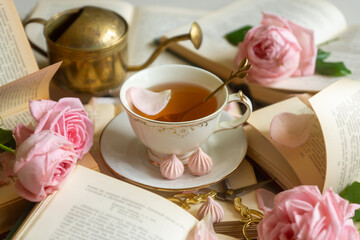 A cup of aromatic tea, a book and a rose on the table.