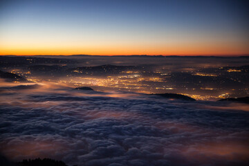 View in the evening from Mount Rigi to Lake Zug, which is covered with a thick layer of fog and the lights of the villages below shine through the fog.