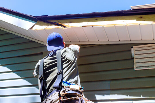 As construction process, an employee installs vinyl plastic siding panels on wall facade of new home