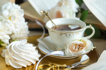 A cup of aromatic tea, a book and a rose on the table. May June July August.