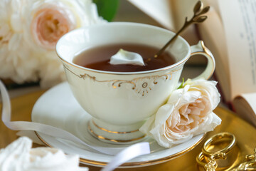 A cup of aromatic tea, a book and a rose on the table. May June July August.