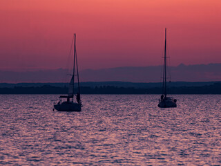 The image captures a serene scene with two sailboats on the water during sunset. 
