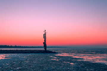 Obraz premium A tranquil sunset paints the sky above a lone tower by the water.