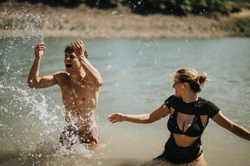 Fototapeta premium Joyful young couple having a fun splash fight in the lake on a sunny day, expressing happiness and carefree moments.