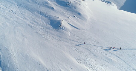 Sportsman people group running winter snow hill trail. Snow-covered slope in Antarctica pristine nature. Men wearing winter gear in cold sunny day. Active sport, tourism, recreation. Aerial top shot