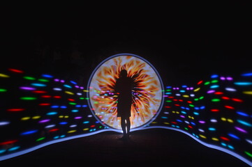 One person standing alone against a Colourful circle light painting as the backdrop	
