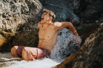 Young man cooling off in the mountain river, enjoying the refreshing water on a sunny day. Refreshing natural setting and summer enjoyment.