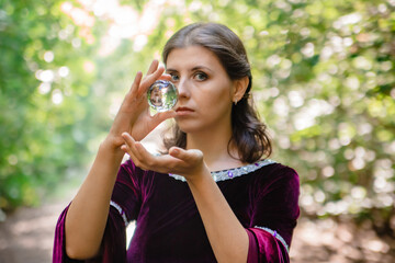 A young woman with brown hair in a medieval dress holds a crystal ball in her hands. Looking into the future, fortune telling