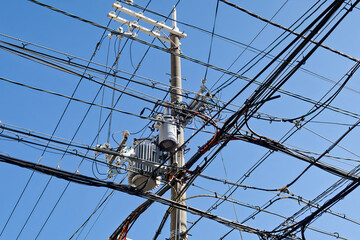 A power line with a pole in the middle. The pole is surrounded by many wires with blue sky.