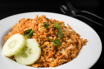 Close up side view photo of Homemade fried rice with vegetables, chicken and fried eggs served on a white plate with spoon and fork. Isolated on black background.