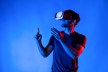 Caucasian man wearing virtual reality goggle while standing at neon light background. Person with...