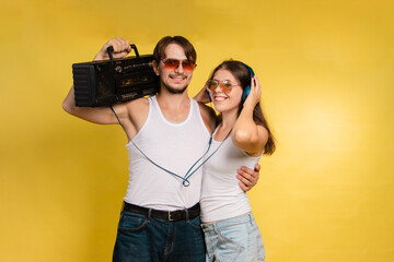 Young man and woman in sunglasses on yellow background. Retro style. Man has retro tape recorder....