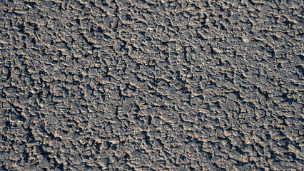 close-up view of a rough asphalt pavement surface. The texture is detailed, revealing the coarse, aggregate composition of the material, with visible cracks and an uneven pattern © Jarama