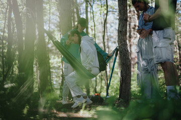 A group of friends spending quality time together in a forest, enjoying nature and relaxation with a hammock. Perfect for concepts related to friendship, leisure, and outdoor activities.