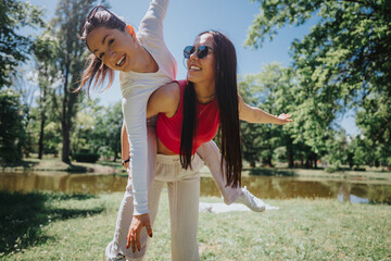 Two young women enjoy a playful piggyback ride in a lush green park, radiating happiness and...