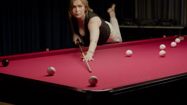Woman leans over an unusual red pool table and strikes the ball with her cue, sending it into the pocket.