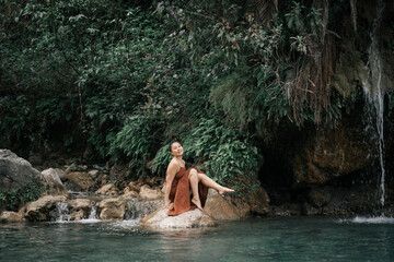  Secret Waterfall. An Asian girl in a brown dress against the backdrop of the tropics.High quality photo