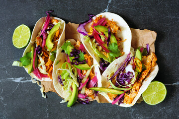 Chicken street tacos with avocado, cabbage slaw and pickled red onions. Top view on a dark stone background.