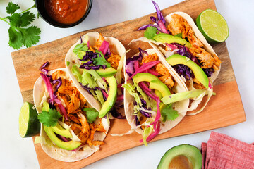 Chicken street tacos with avocado, cabbage slaw and pickled red onions. Top view table scene with platter on a white marble background.