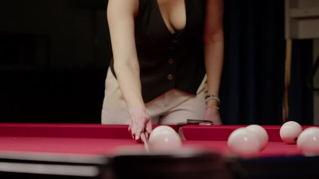 Woman practices in a nightclub by playing billiards. She arranges the balls in a line to practice her shot. Close up. Slow motion