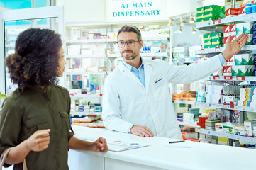 Man, pharmacist and shelf with customer for medication, option or choice at pharmacy. Mature medical employee talking to shopper and showing inventory, stock or pharmaceutical drugs at dispensary