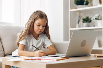 Young girl focused on online learning, sitting at a table with a laptop and pen, studying diligently