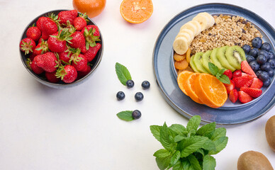 Granola with strawberries, kiwi, banana and blueberries in a round plate on a white table. Healthy and tasty food