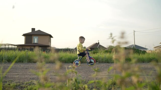 Summer, child, bike on the road. A little boy rides a tricycle. A child in a T-shirt rides a tricycle along the road in a new village.