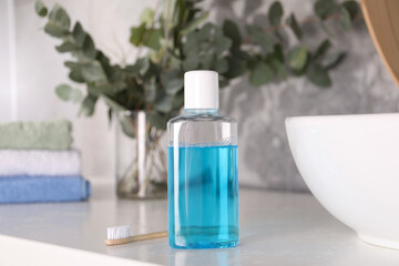 Bottle of mouthwash and toothbrush on white table in bathroom