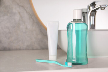 Bottle of mouthwash, toothpaste and toothbrush on light countertop in bathroom