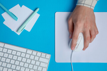 Man working with mouse, computer keyboard and stationery at light blue table, top view