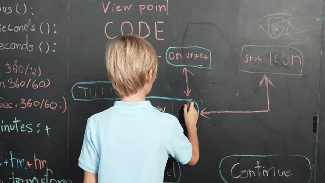 Back view of student writing engineering prompt on blackboard. Handsome clever child or boy planing a project by using coding and programing system in STEM technology classroom. Closeup. Erudition.