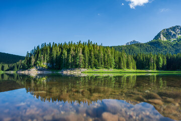 Der schwarze See oder Crno Jezero ist ein Gletschersee und ein Higlight in Durmitor in Montenegro, im Hintergrund die Berge mit Bäumen und Wald, im Vordergrund Reflexionen im Wasser