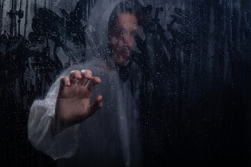 Portrait of Man wearing raincoat behind wet glass. Touching the glass with your hand. Studio portrait.